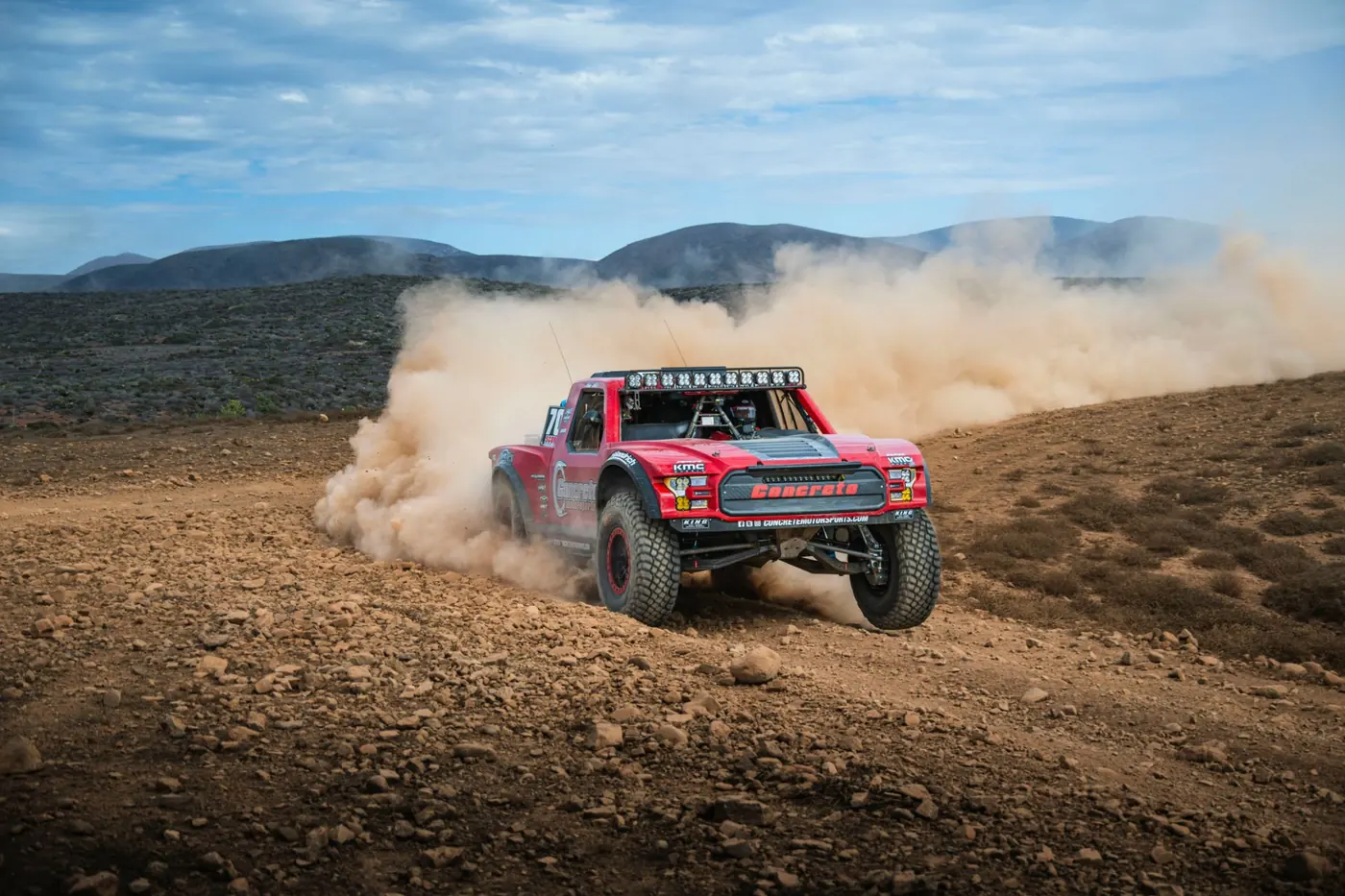 An off-road truck kicking up dust on a rocky trail